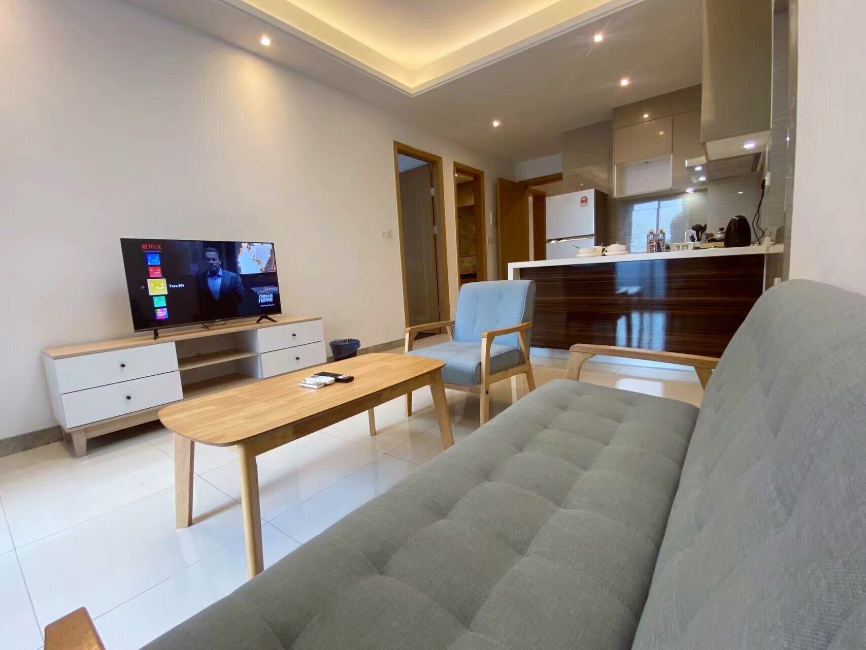 A modern living room with a sofa, a coffee table, a TV, and a kitchen area in the background.