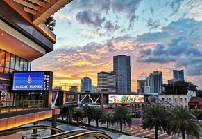 A cityscape with modern buildings, a prominent sign for Daulat Tuanku, and a sunset sky.