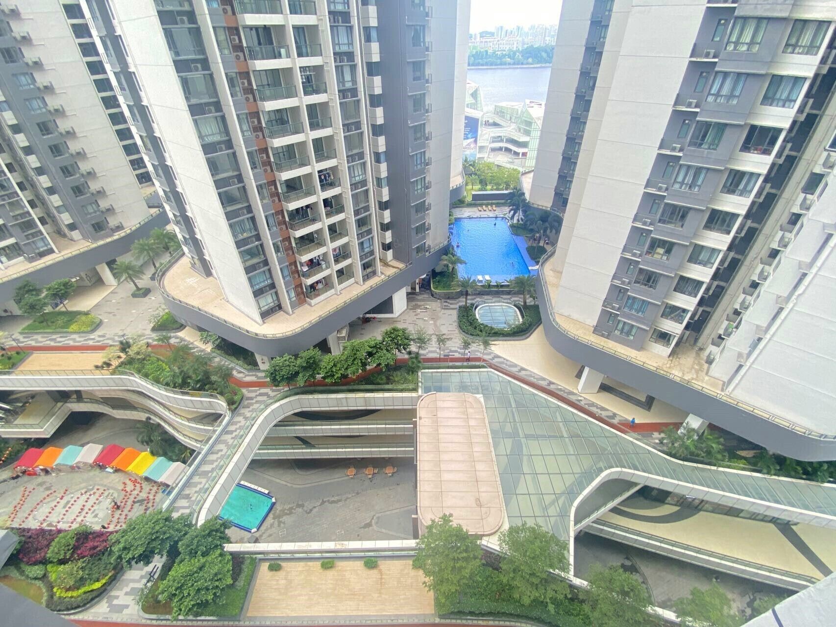 A high-rise residential building with multiple balconies, a central swimming pool, and a pedestrian bridge.
