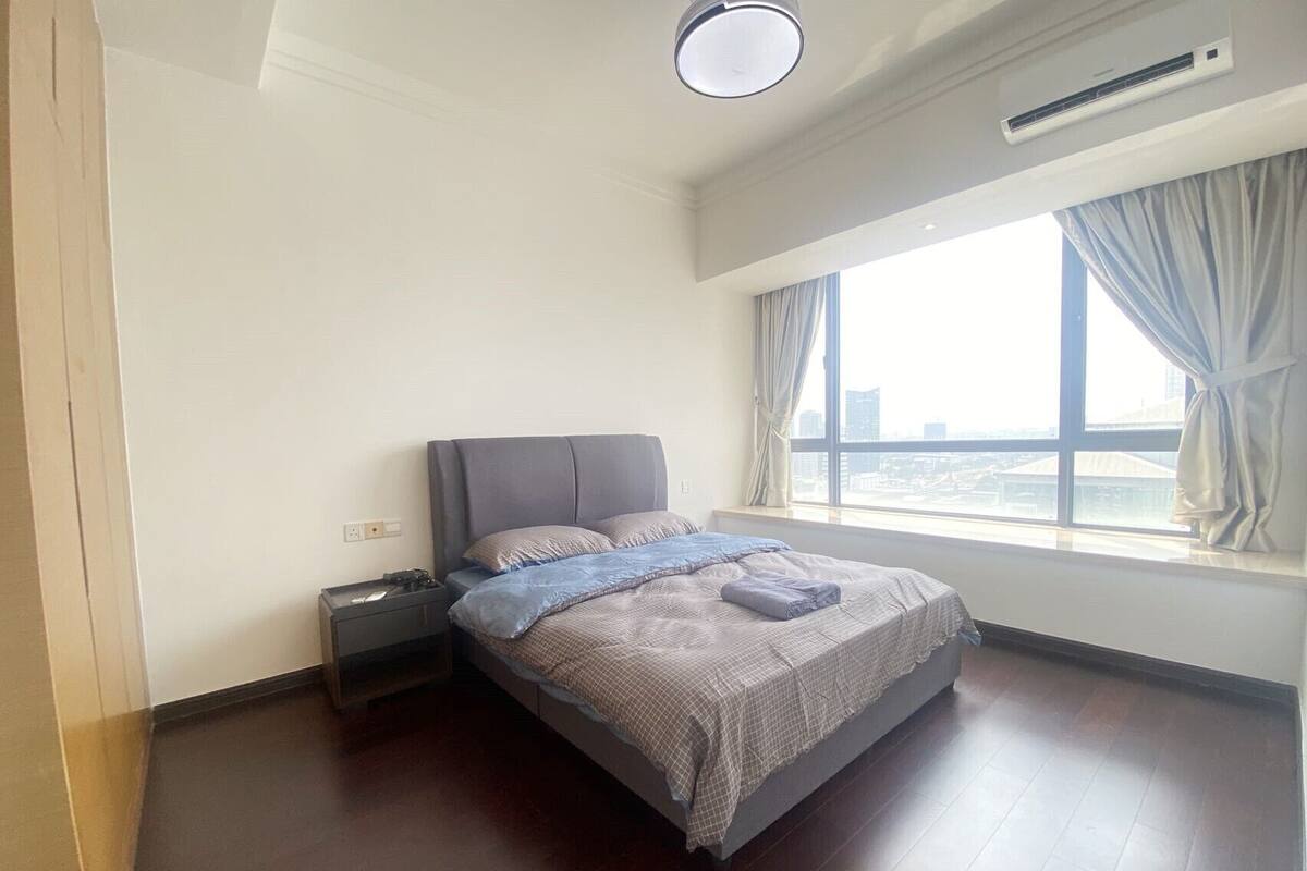 Une chambre à coucher comprenant un lit, une table de chevet, un appareil de climatisation et une fenêtre avec des rideaux.