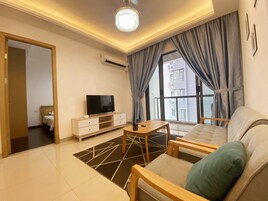 Una sala de estar moderna con un sofá, un televisor sobre un mueble, una mesa de centro y vistas de la ciudad a través de amplias ventanas.