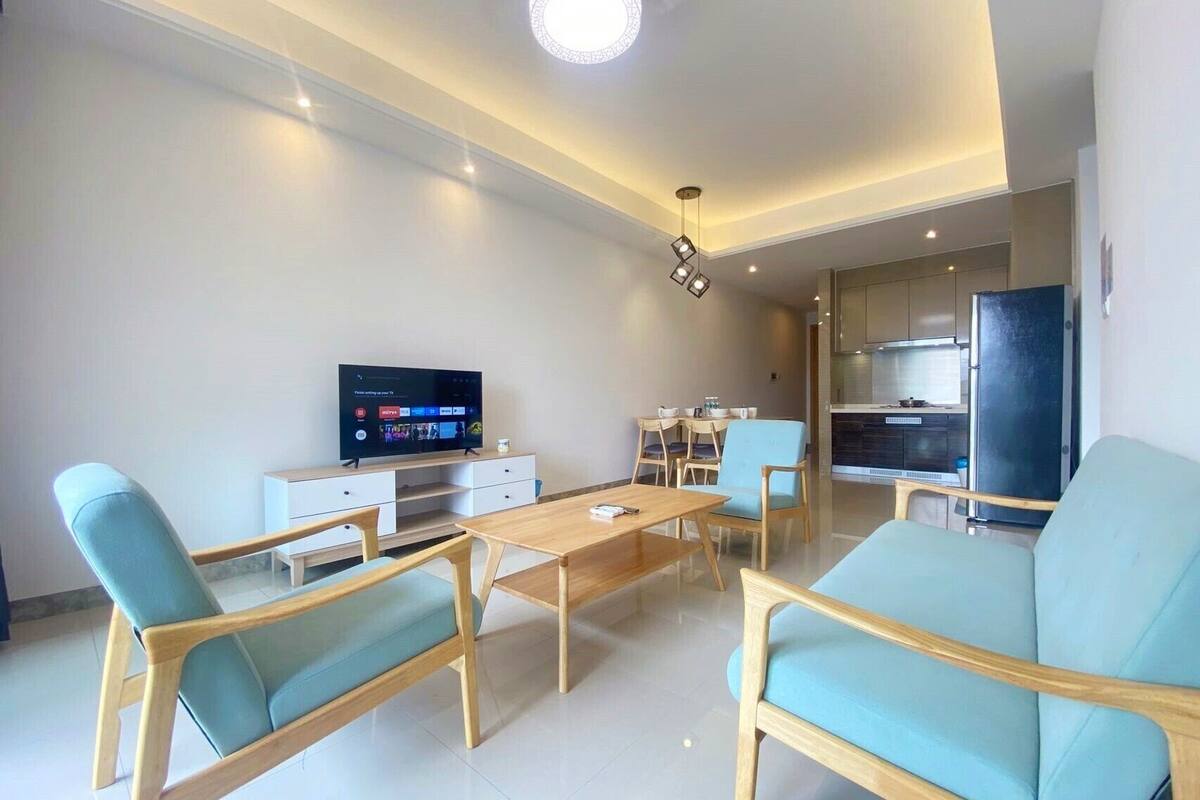 Un salon moderne doté d’un téléviseur à écran plat, de meubles en bois et d’un coin cuisine.