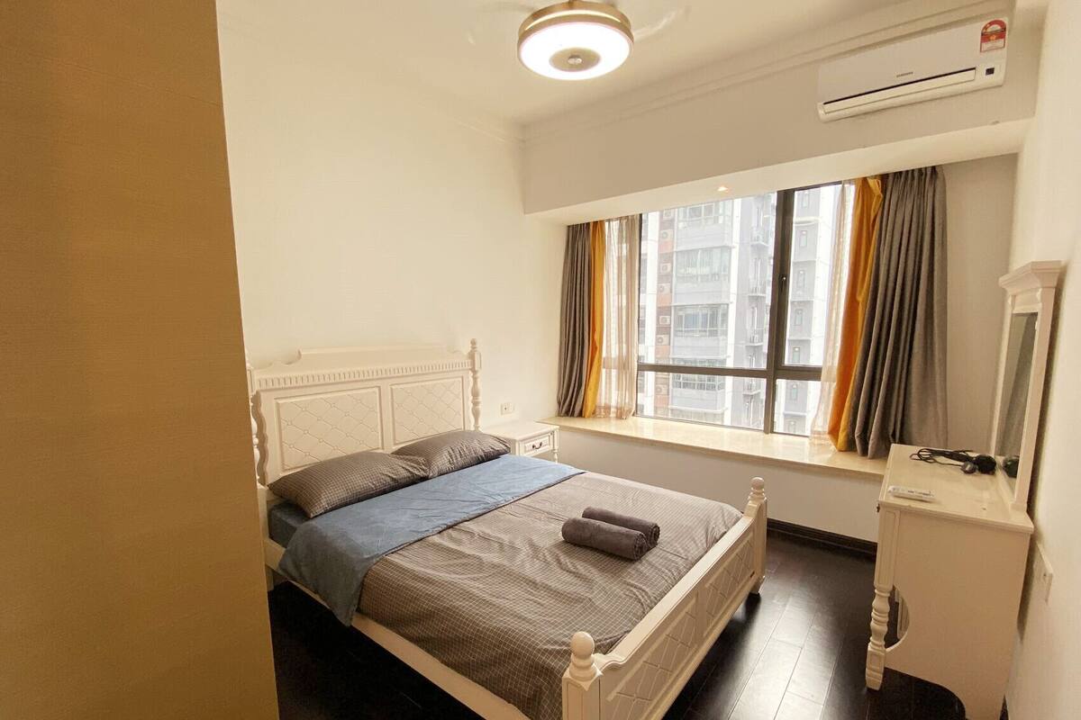 Une chambre à coucher avec un lit, une fenêtre avec des rideaux, une table de chevet et un appareil de climatisation.