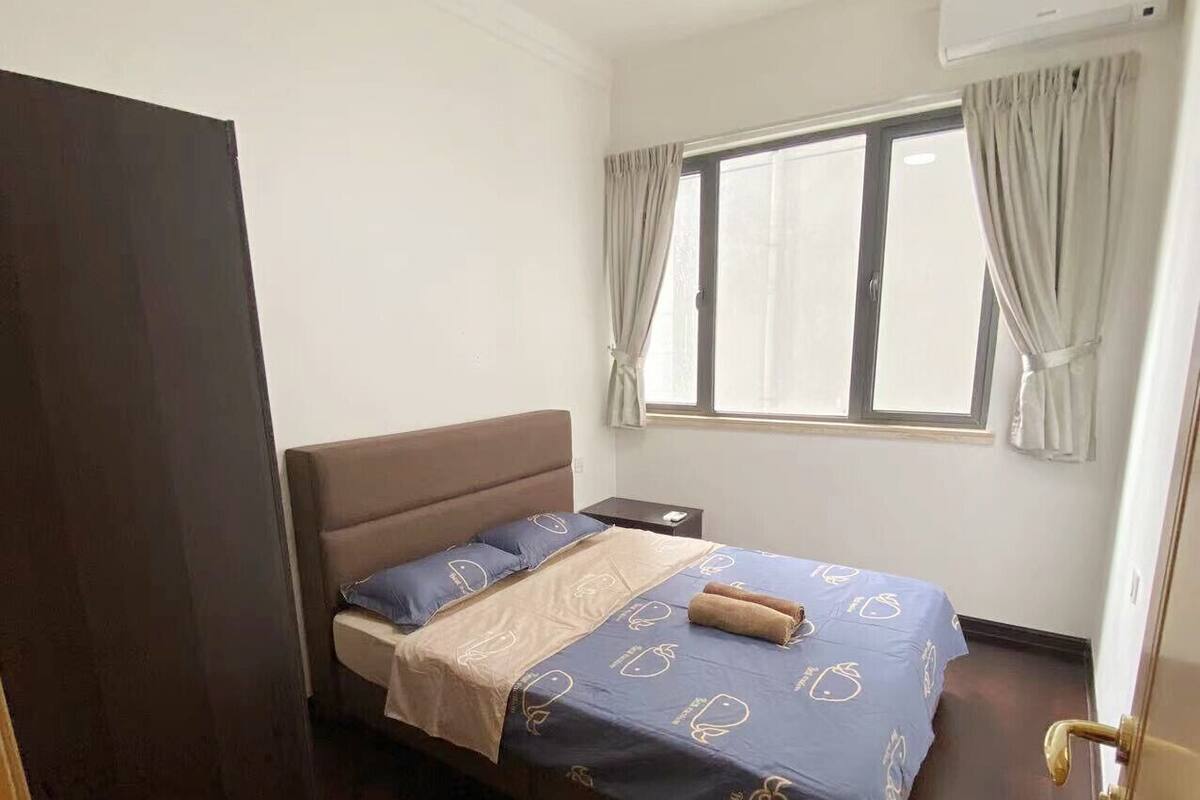 Une chambre à coucher comprenant un lit, un ventilateur de plafond, une fenêtre avec des rideaux et un appareil de climatisation.