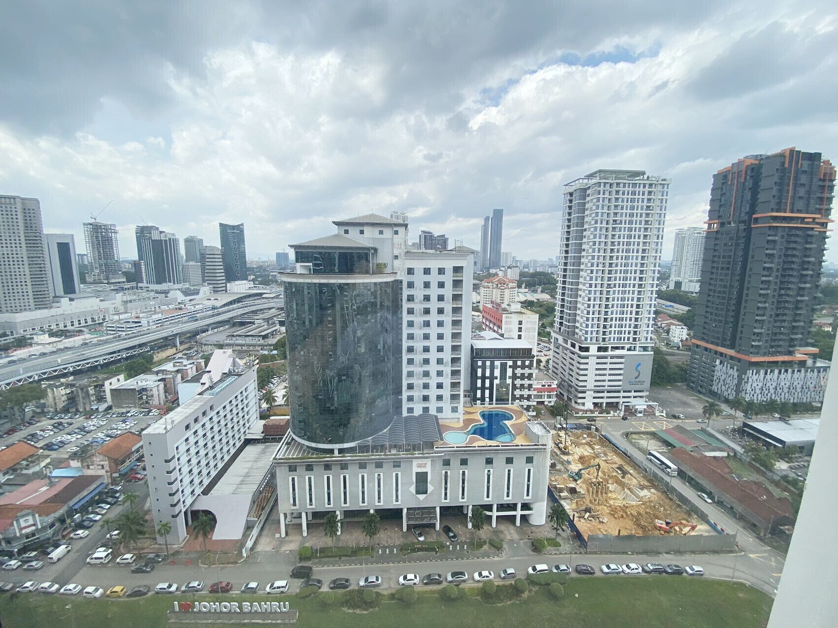 A modern building with a unique curved facade, surrounded by high-rise buildings and a busy street with cars.
