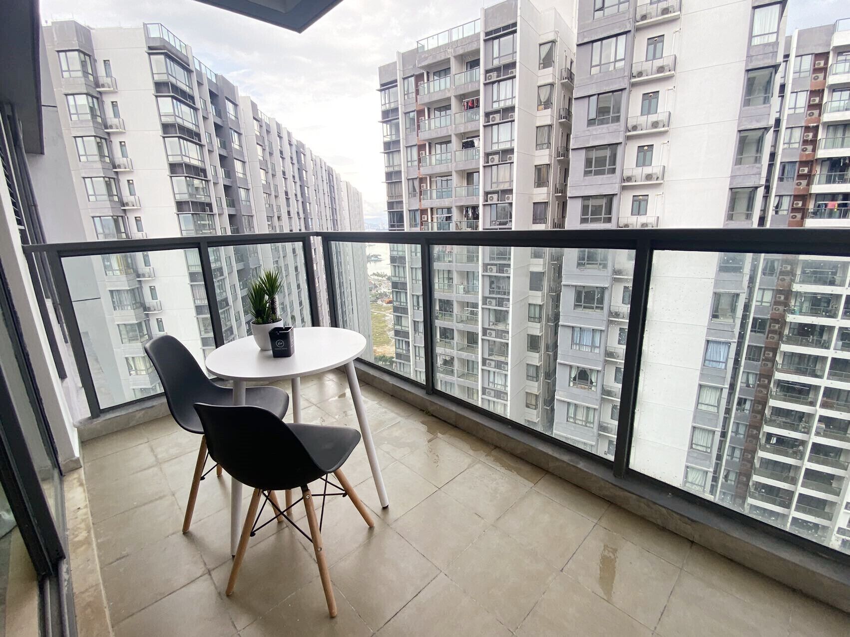 A balcony with a table and chairs, a potted plant, and a view of high-rise buildings.