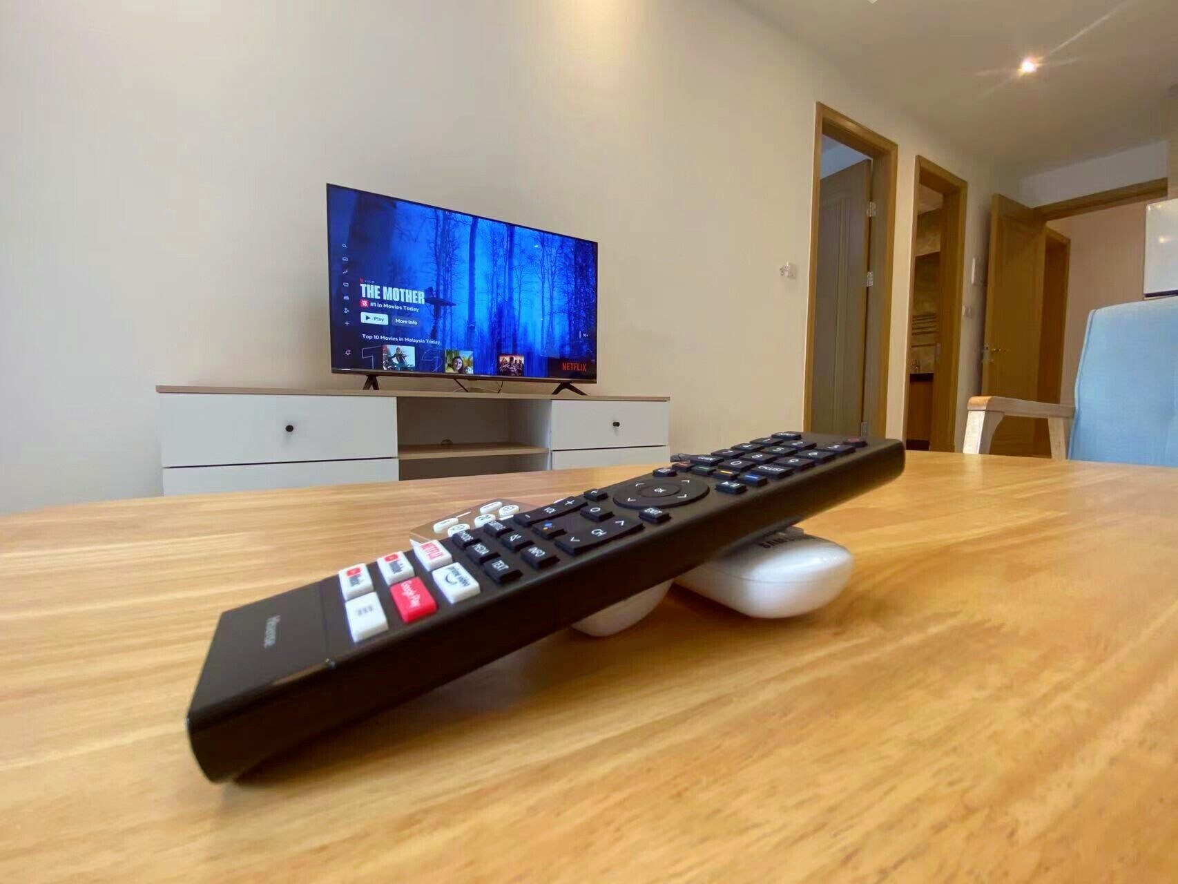 A remote control on a wooden table with a television displaying 'The Mother' in the background.