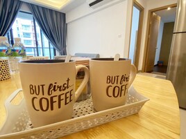 Two coffee mugs on a tray with the text "BUT first... COFFEE" in a room with a window, curtains, and a refrigerator in the background.