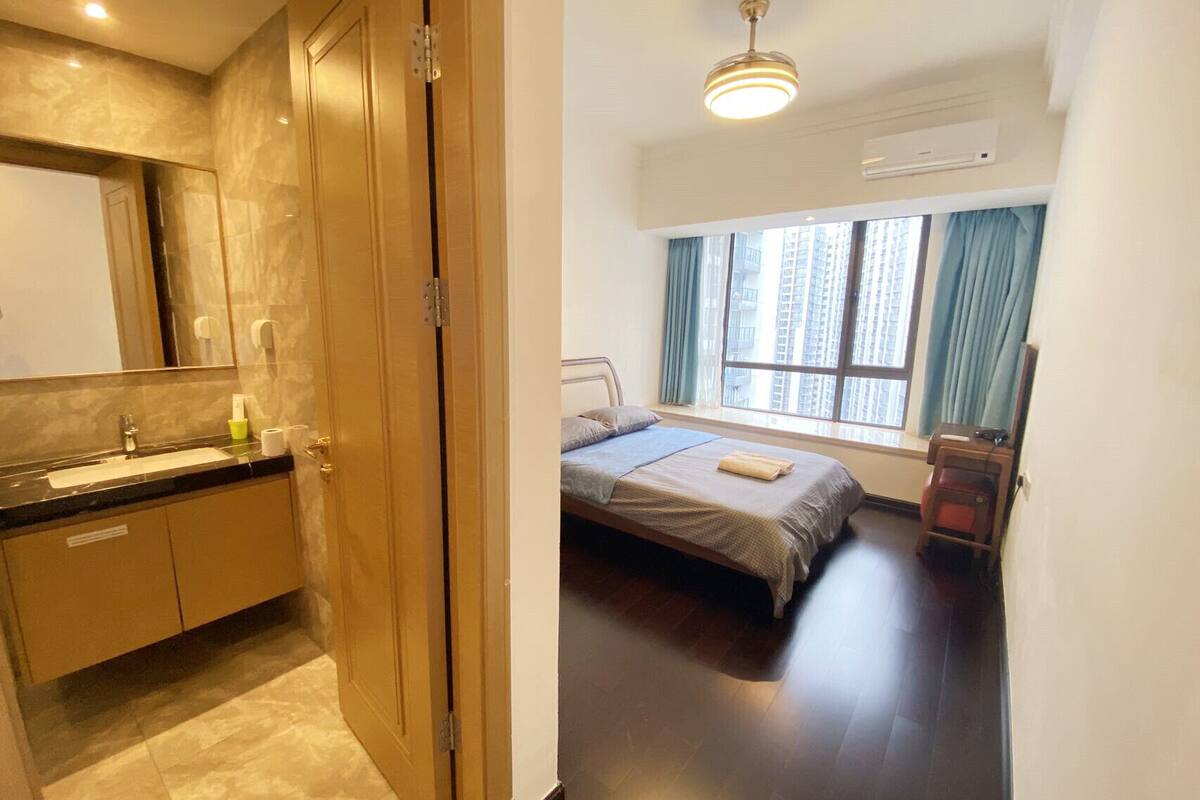 Une chambre d’hôtel avec un lit, une fenêtre avec des rideaux, une salle de bain avec un miroir et un luminaire au plafond.