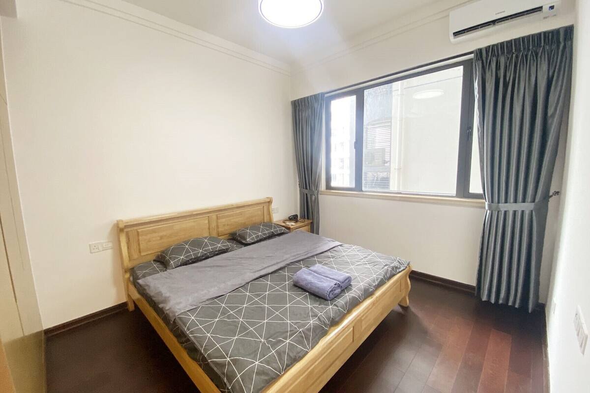 Une chambre avec un lit en bois, une fenêtre avec des rideaux, un climatiseur et un luminaire au plafond.