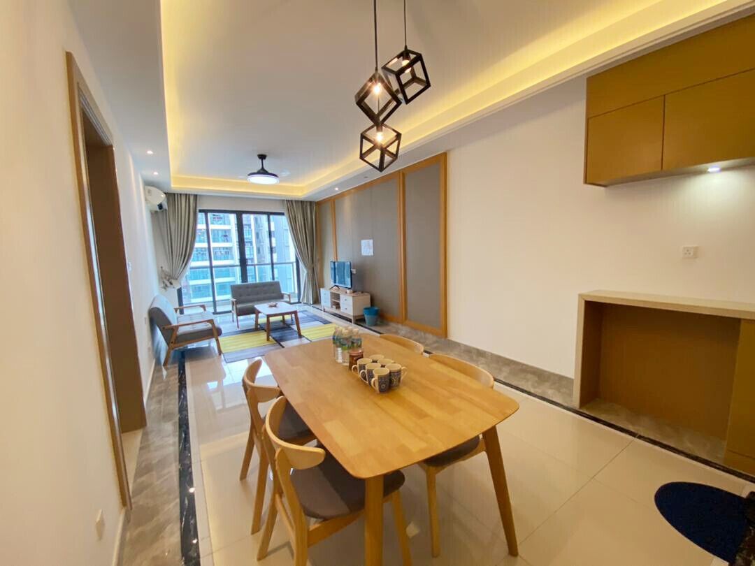 Un comedor moderno con una mesa y sillas de madera, un ventilador de techo y vistas a la ciudad a través de amplios ventanales.