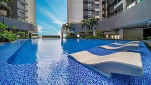 A swimming pool with blue mosaic tiles, surrounded by modern buildings and palm trees. - R&F TrexHomestay (Johor Bahru)