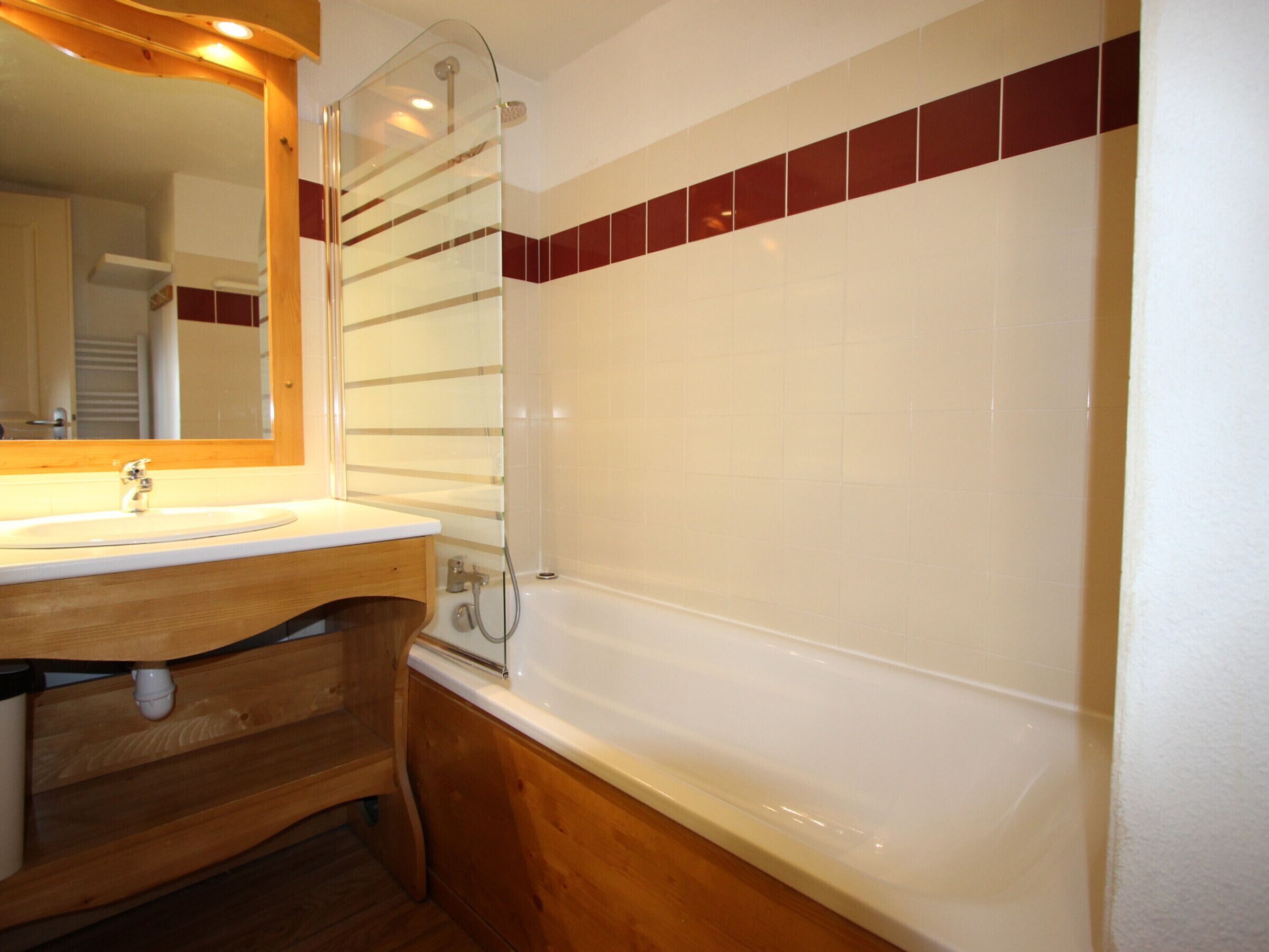 A bathroom with a wooden vanity, a sink, a mirror, and a bathtub.
