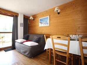 A cozy room with a grey sofa, wooden walls, a dining table with chairs, and a framed picture on the wall.