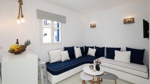 A modern living room with a white sofa, blue cushions, a small round table, and a fruit bowl on a white cabinet. - Hyades - Downtown Suites No 1 , Mykonos Town (Mykonos Town Cyclades)