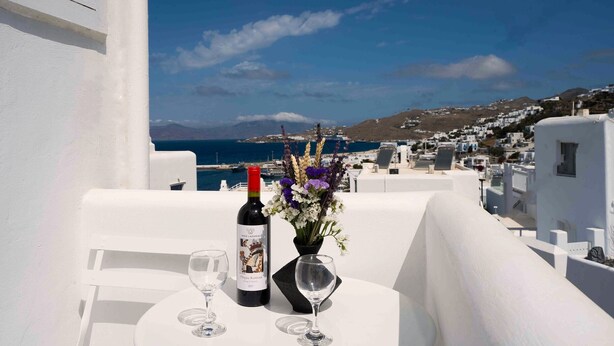 A table with a bottle of wine and a vase of flowers on a balcony overlooking a coastal town. - Hyades - Downtown Suites No 1 , Mykonos Town (Mykonos Town Cyclades)