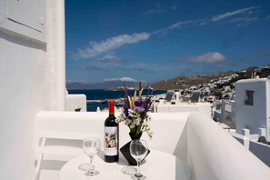 A table with a bottle of wine and a vase of flowers on a balcony overlooking a coastal town.