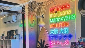 Une pièce décorée d’un panneau néon avec des inscriptions dans plusieurs langues, d’une planche de surf et d’une table sur laquelle sont posés des magazines.