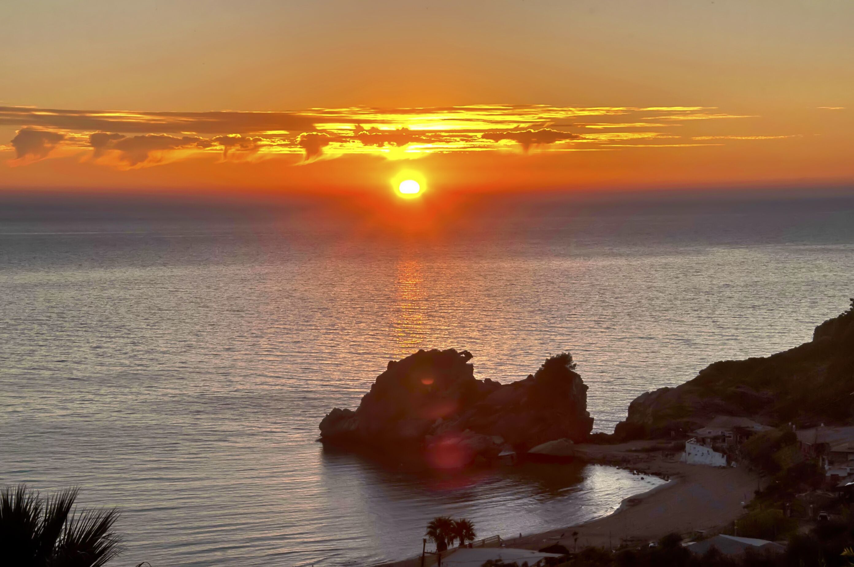 Ein Küsten-Sonnenuntergang mit einem Felsvorsprung im Vordergrund und ruhiger See.