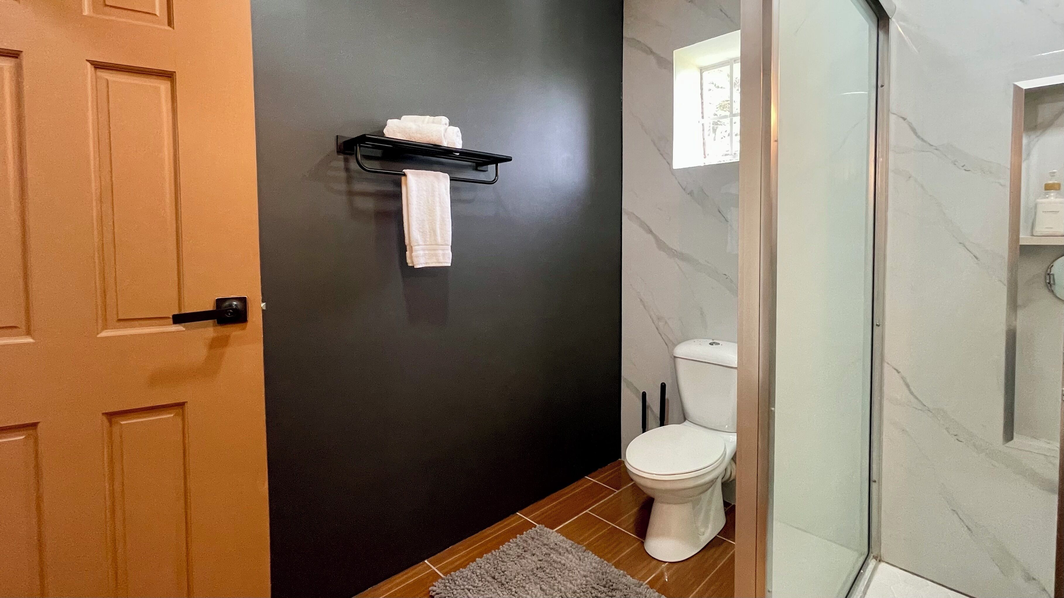 Um banheiro com parede escura, vaso sanitário branco, porta-toalhas e área de chuveiro.