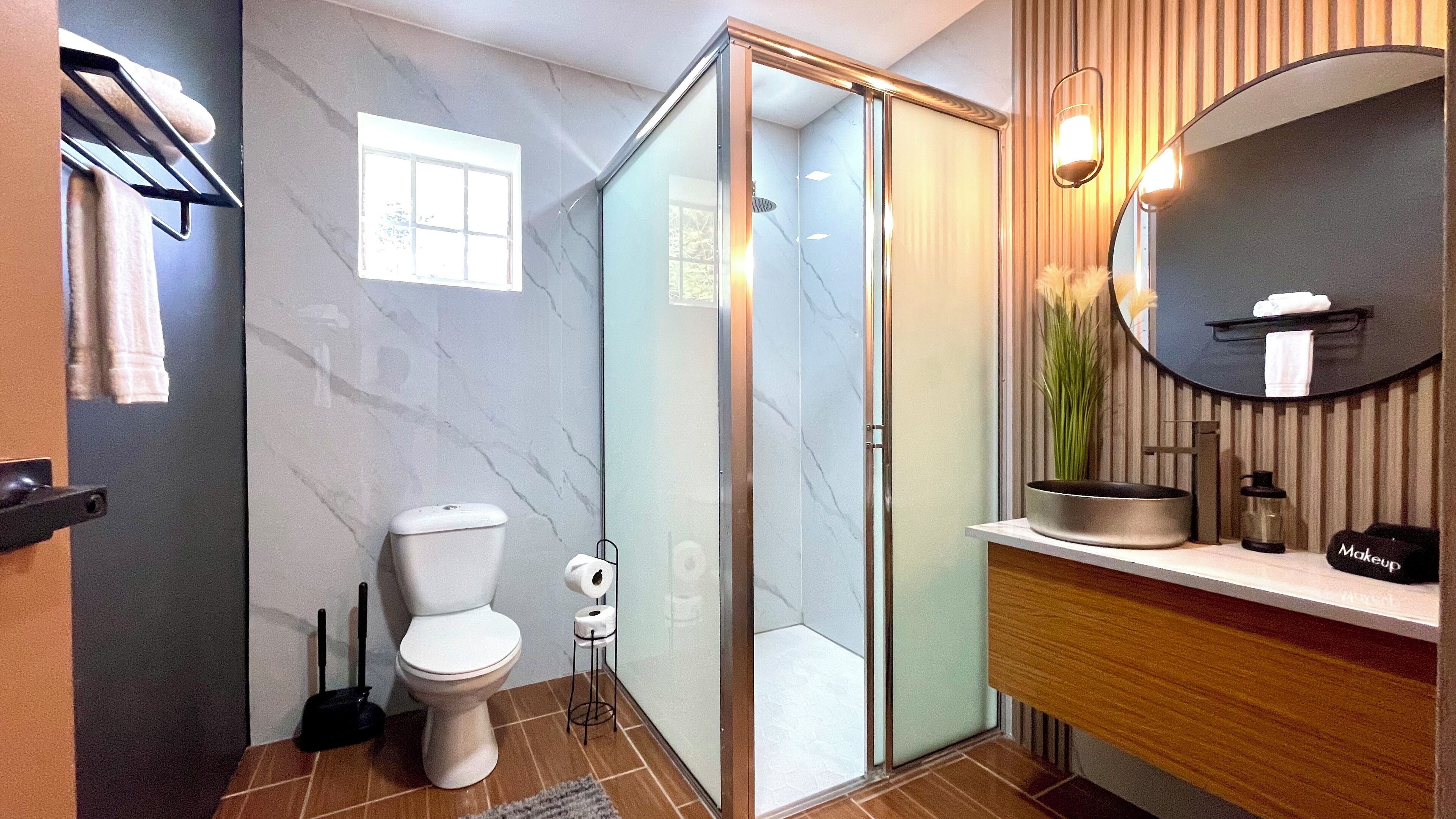 A modern bathroom with a glass shower enclosure, a toilet, a sink with a mirror, and a towel rack.
