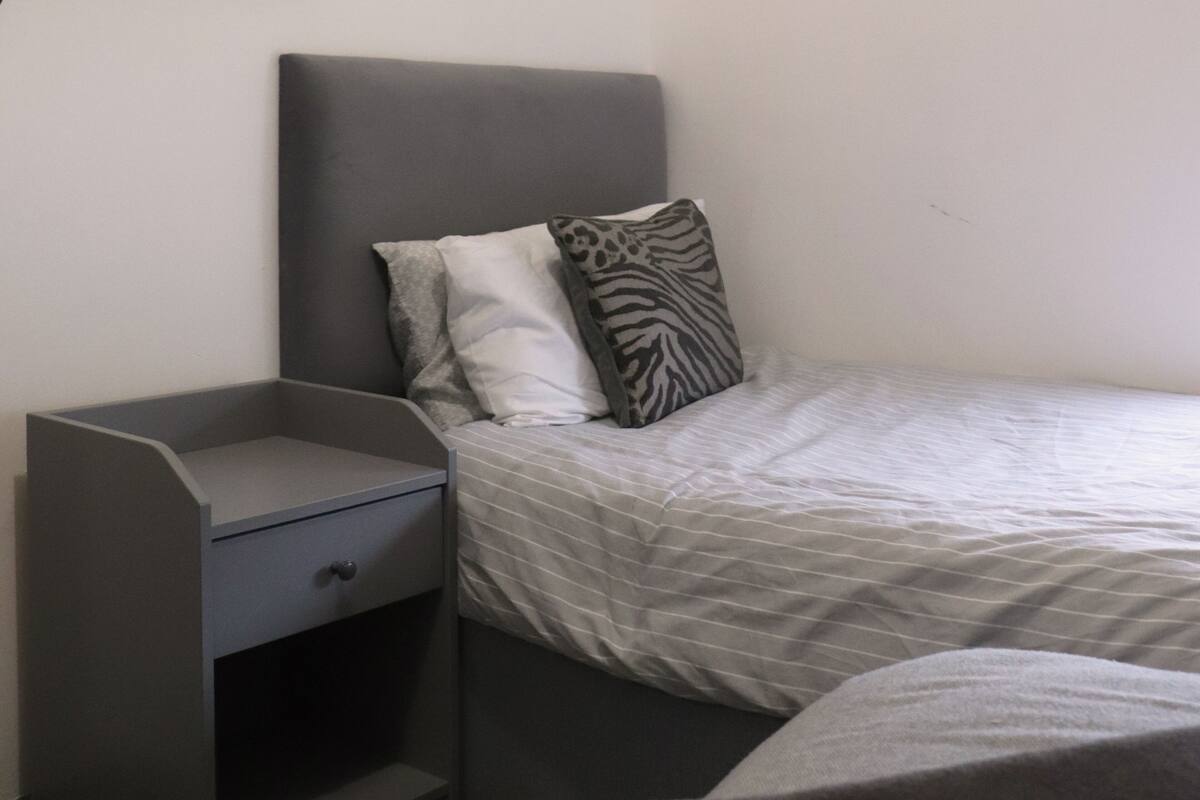 A small, compact bedroom with a single bed, a nightstand, and a built-in storage unit.
