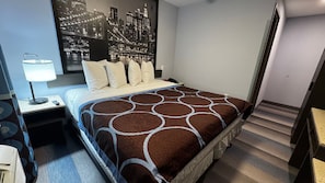Une chambre d’hôtel avec un lit, une table de chevet, une lampe et une fresque murale représentant un paysage urbain.