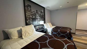 A hotel room with two beds, a nightstand, a cityscape artwork on the wall, and a wooden floor.