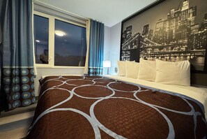 Ett hotellrum med en stor säng, en väggmålning som föreställer en stadsbild, ett fönster med gardiner och utsikt över natthimlen.