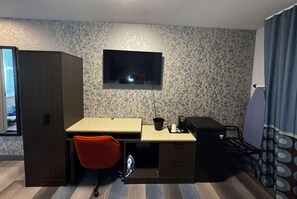 Une pièce de taille modeste comprenant un bureau, une chaise, un téléviseur, une armoire et un lit.