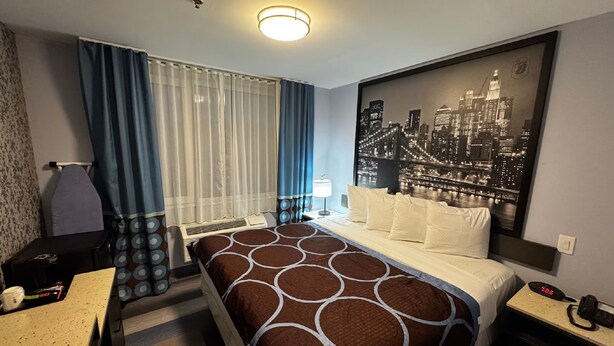 Une chambre d’hôtel équipée d’un lit, d’un bureau, d’une chaise, d’une table de chevet, d’une lampe et offrant une vue sur le paysage urbain.