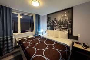 A hotel room with a bed, a window with curtains, a cityscape artwork on the wall, a nightstand with a phone, and a wall socket. - Super 8 By Wyndham Brooklyn Fulton Street (Brooklyn)