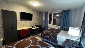 Une chambre d’hôtel avec deux lits, un bureau, une chaise, une télévision et une fenêtre avec des rideaux.
