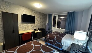 Ett hotellrum med två sängar, ett skrivbord, en stol, en TV och ett fönster med gardiner.