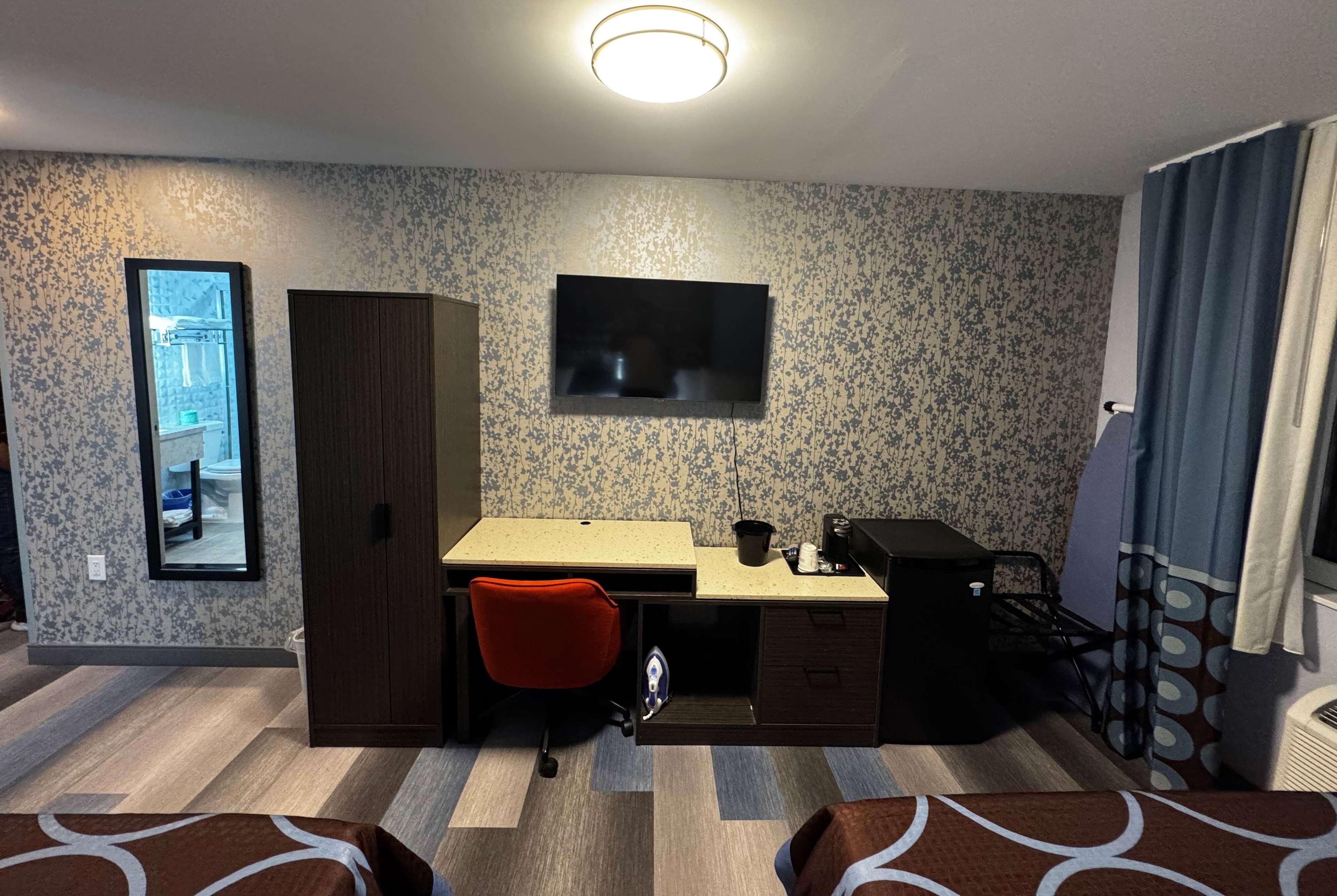A compact hotel room with a bed, a desk with a chair, a television, and a wardrobe.