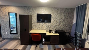 A compact hotel room with a bed, a desk with a chair, a television, and a wardrobe.
