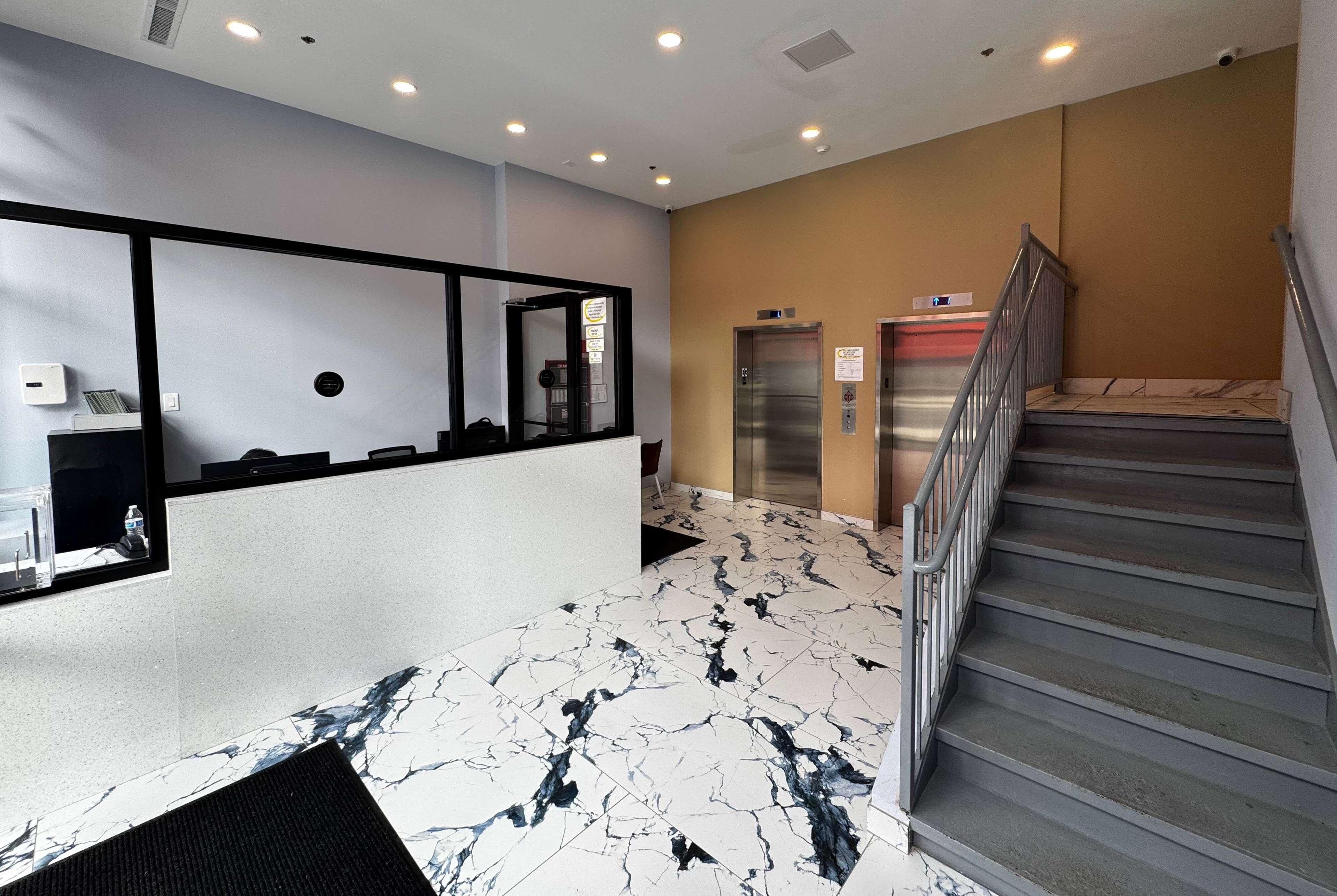 A hotel lobby with a reception desk, a marble floor, a staircase, and two elevators.