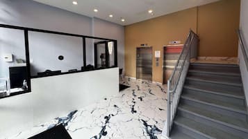 A hotel lobby with a reception desk, a marble floor, a staircase, and two elevators.