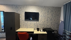 A small room with a TV mounted on the wall, a desk with a chair, a small kitchenette, and a wardrobe. - Super 8 By Wyndham Brooklyn Fulton Street (Brooklyn)