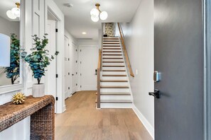 A hallway with a wooden staircase, white doors, and a bench with decorative items. - Luxe Downtown Home • DT ~2m • Rooftop • Fireplace (Nashville)