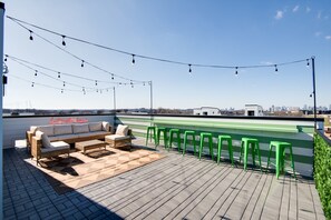 A rooftop terrace with a sofa set, green bar stools, and string lights. - Luxe Downtown Home • DT ~2m • Rooftop • Fireplace (Nashville)