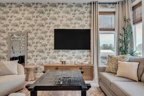 A living room with floral wallpaper, a large flat-screen TV, a wooden cabinet, and a sofa with cushions.