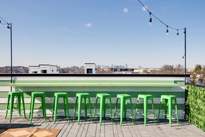 A rooftop bar with green stools and a city view.