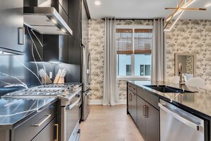 A modern kitchen with stainless steel appliances, a black countertop, and a window with blinds. - Luxe Downtown Home • DT ~2m • Rooftop • Fireplace (Nashville)