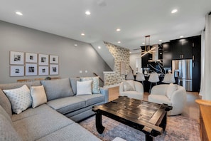 A modern living room with a grey sectional sofa, a wooden coffee table, and a dining area with a white chair and lamp.