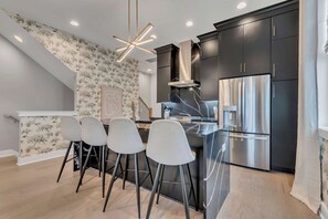 A modern kitchen with dark cabinetry, stainless steel appliances, and a central island with bar stools.