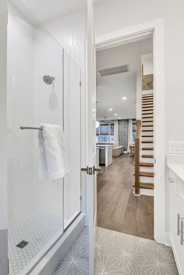 A modern bathroom with a glass shower enclosure, a white towel hanging on the door, and a patterned floor.