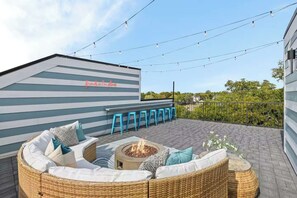 A rooftop patio with a fire pit, outdoor seating, and string lights.