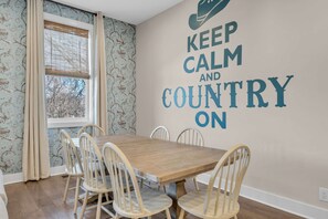 Rustic dining area featuring a large wood table, spindle chairs, and a playful "Keep Calm and Country On" wall mural. - Luxe Downtown Home • Rooftop • Fireplace • DT ~2m (Nashville)