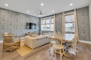 A modern living room with a sofa, dining table, chairs, a TV, and a ceiling fan.